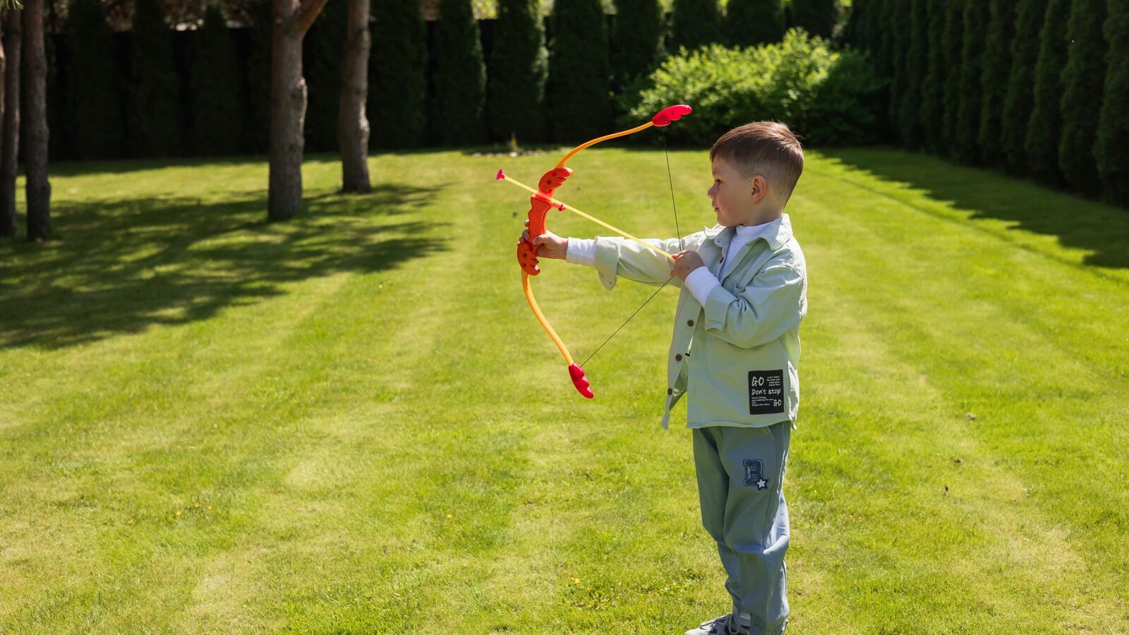 Jeune garçon jouant avec un arc et des flèches en plastique sur une pelouse